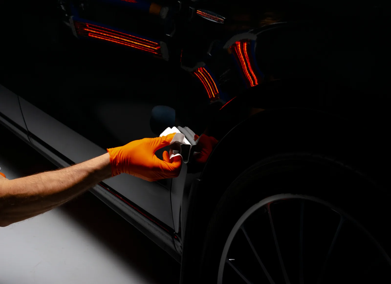 A gloved hand applying ceramic coating by hand to the rear quarter panel of a black car.